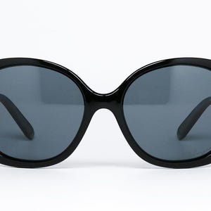 Puede incluir: Gafas de sol negras con montura grande y redondeada y lentes gris oscuro. Las gafas de sol tienen un dise&ntilde;o cl&aacute;sico de gran tama&ntilde;o, adecuado para varias formas de rostro. Las patillas son elegantes y negras, proporcionando un aspecto cohesivo. Accesorio de moda.