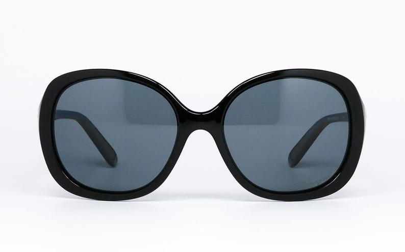 Puede incluir: Gafas de sol negras con montura grande y redondeada y lentes gris oscuro. Las gafas de sol tienen un dise&ntilde;o cl&aacute;sico de gran tama&ntilde;o, adecuado para varias formas de rostro. Las patillas son elegantes y negras, proporcionando un aspecto cohesivo. Accesorio de moda.