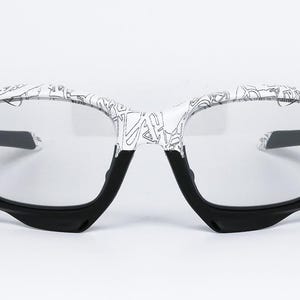 May include: Eyeglasses with a white frame featuring a black and white graphic design. The lower portion of the frame and the temples are black. The lenses are clear.