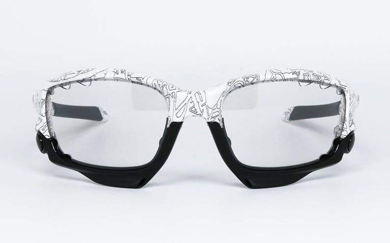 May include: Eyeglasses with a white frame featuring a black and white graphic design. The lower portion of the frame and the temples are black. The lenses are clear.