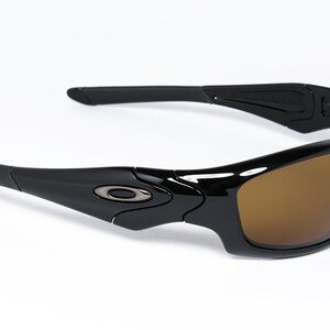 May include: Black sunglasses with brown lenses. The sunglasses have a sleek, modern design with a glossy finish. The Oakley logo is visible on the temples. Suitable for sports and outdoor activities.