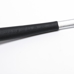 May include: Close-up of a tool with a black handle and a silver metal shaft. The black handle has the words "MADE IN U.S.A." embossed on it. The tool is set against a white background.