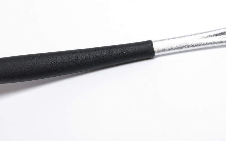 May include: Close-up of a tool with a black handle and a silver metal shaft. The black handle has the words "MADE IN U.S.A." embossed on it. The tool is set against a white background.
