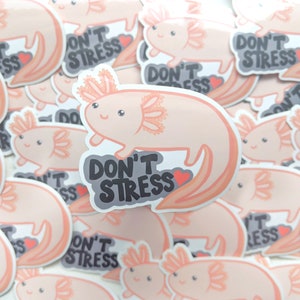 May include: A collection of stickers featuring a cartoon axolotl in shades of peach and pink. Each sticker has the text "DON'T STRESS" in a gray bubble with a red heart. The axolotl has a smiling face and detailed gills.