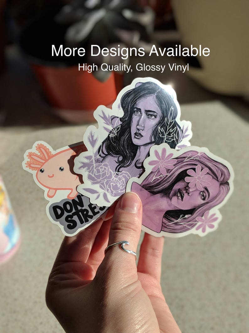 May include: A hand holding a collection of glossy vinyl stickers. The stickers feature illustrations of a woman, an axolotl, and the words "DON'T STRESS". The text "More Designs Available" and "High Quality, Glossy Vinyl" are also visible.