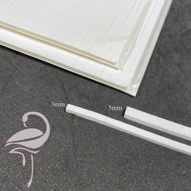 May include: Two white foam strips, one measuring 3 mm and the other 5 mm, are shown on a dark gray surface. The foam strips are used for crafting and scrapbooking.