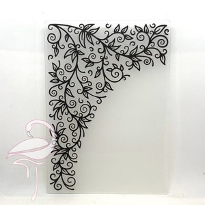 May include: A rectangular clear glass cutting board with a black floral design in the upper left corner. The design features leaves and swirling vines. The board is ideal for kitchen use.