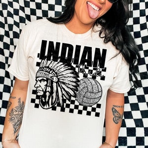 May include: White t-shirt with a black and white graphic design featuring a Native American headdress, a volleyball, and a checkered pattern. The text "INDIAN Pride" is written on the shirt.