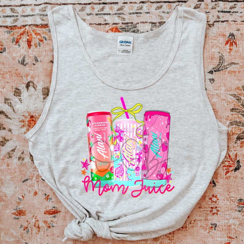 Pu&ograve; includere: Canotta grigio chiaro con una grafica colorata di tre bevande. I contenitori sono rosa e bianchi, con il testo "Alani" e "Mom Juice" in rosa. Il design include stelle e frutta.