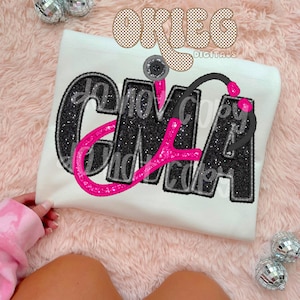 Puede incluir: Una camiseta blanca con un diseño de purpurina negra y rosa que dice "CNA" con un estetoscopio en la parte superior. El diseño está rodeado por un borde a cuadros marrón y blanco. El texto "Okie Digitals" está en la esquina superior derecha de la imagen.