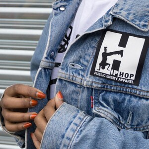 May include: A blue denim jacket with a white patch that says "Hip Hop Public Enemy Apparel" and features a silhouette of a person doing a handstand.