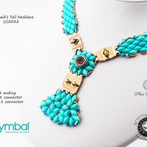 May include: A turquoise and gold beaded necklace with a mermaid's tail design. The necklace features a large, decorative flower-shaped pendant in the center. The text "Mermaid's Tail Necklace (c)2022" is visible at the top of the image.