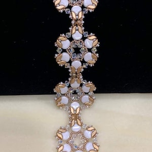 May include: A white and gold beaded bracelet with a flower design. The bracelet is made with small, round beads and has a gold clasp.