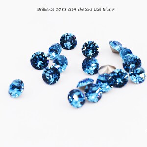 May include: A group of blue crystal rhinestones, known as chatons, are scattered on a white surface. The rhinestones are round and have a faceted design. The text "Brilliance 1088 ss39 chatons Cool Blue F" is visible at the top of the image.