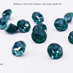 May include: A close-up of ten teal blue round glass rhinestones, also known as chatons, scattered on a white surface. The text "Brilliance 1088 ss39 chatons, Pine Green Ignite UF" is visible at the top of the image.