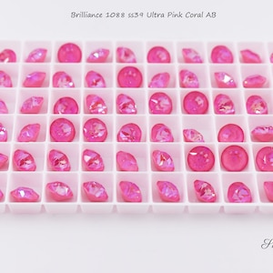 May include: A tray of 36 pink iridescent rhinestones in a grid pattern. Brilliance 1088 ss39 Ultra Pink Coral AB.