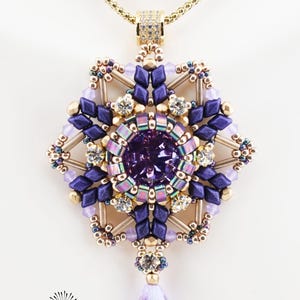 Puede incluir: Collar con un colgante detallado. El colgante presenta una piedra preciosa púrpura central, rodeada por un diseño de estrella de cuentas púrpuras y doradas, y cristales transparentes. El texto "Clandestine Pendant (c)2025 Purple/champagne" es visible.