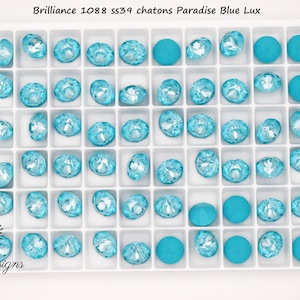 May include: A white tray filled with various Paradise Blue Lux chatons. The tray contains round and oval-shaped crystal rhinestones, along with round, solid-colored beads. The text "Brilliance 1088 ss39 chatons Paradise Blue Lux" is at the top.