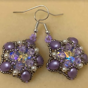 May include: A pair of purple and silver earrings with a star-shaped design. The earrings are made with beads and crystals.