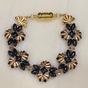 May include: A black and gold beaded bracelet with a magnetic clasp. The bracelet features a repeating pattern of black and gold beads arranged in a flower shape.