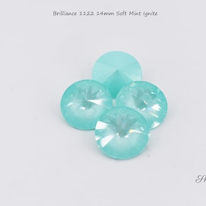 May include: Four 14mm soft mint ignite rhinestones. The rhinestones are round and have a faceted design. They are a light blue color with a slight iridescent sheen.