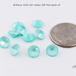 May include: A close-up of a group of small, light blue, faceted rhinestones. The rhinestones are arranged in a semi-circle and are about the size of a US quarter.