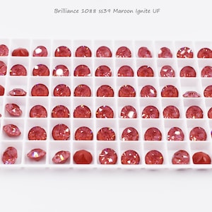 Puede incluir: Una bandeja de 49 piedras de cristal rojas iridiscentes en un patrón de cuadrícula. Las piedras de cristal están etiquetadas como "Brilliance 1088 SS39 Maroon Ignite UF".
