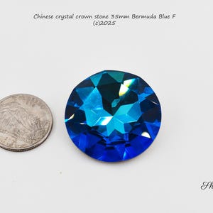 Pode incluir: Uma pedra de coroa de cristal azul de 35 mm, também conhecida como chaton, com um design facetado. A pedra é mostrada ao lado de uma moeda de 1 euro para comparação de tamanho.