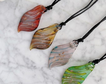 Puede incluir: Cuatro colgantes de hoja de vidrio en cordones negros. Las hojas son en tonos de rojo, amarillo, rosa y verde con motas doradas.