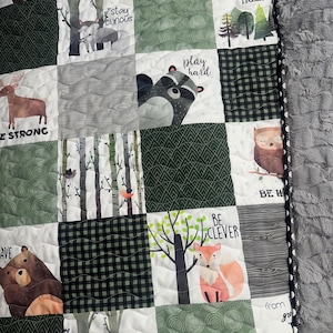 May include: A green and white patchwork quilt with various woodland animal illustrations and inspirational phrases like "stay curious", "play hard", "be clever", and "grow mighty trees".