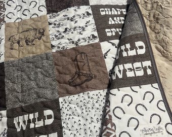 May include: A patchwork quilt with a Wild West theme. The quilt is made of various fabrics with different patterns, including horseshoes, arrows, and the words "Wild West".