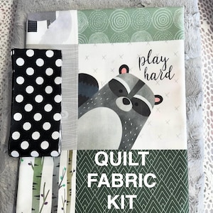 May include: A quilt fabric kit featuring a raccoon with the text "play hard" and a green and white geometric pattern. The kit also includes a black and white polka dot fabric.