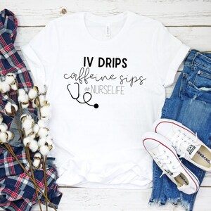 May include: White t-shirt with black text that reads "IV DRIPS caffeine sips #NURSELIFE" and a black stethoscope graphic.