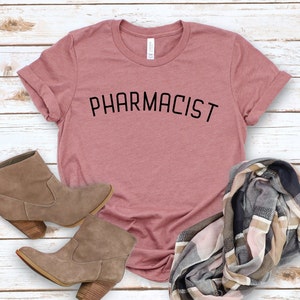 May include: A mauve t-shirt with the word "PHARMACIST" printed in black on the front.