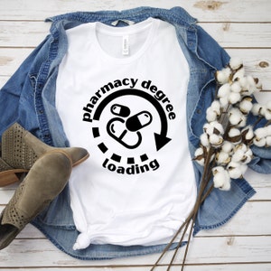 May include: White t-shirt with a black graphic of a loading bar with the text "pharmacy degree loading" and a graphic of three pills.