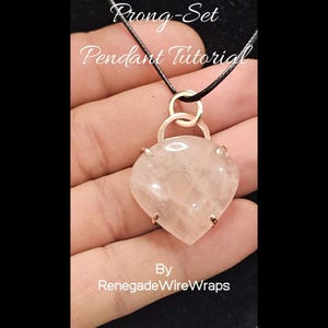 Può includere: Un ciondolo a forma di cuore con una pietra rosa chiaro incastonata a griffe. Il ciondolo è attaccato a un cordino nero.