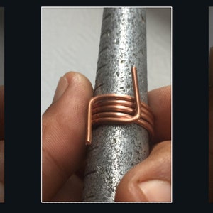 Könnte beinhalten: Ein handgefertigter Kupferdrahtring wird auf einem Metallringgrößenmesser gezeigt. Der Ring hat mehrere Windungen aus Kupferdraht mit einem einzigartigen, eckigen Design. Der Ring hat eine warme Kupferfarbe.