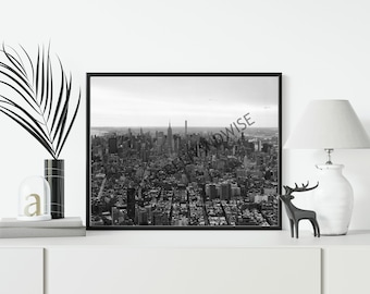 Pode incluir: Fotografia emoldurada a preto e branco de uma paisagem urbana, com inúmeros arranha-céus e edifícios. O Empire State Building é visível. A fotografia é exibida numa superfície branca, juntamente com itens decorativos, incluindo uma lâmpada e uma figura de veado.