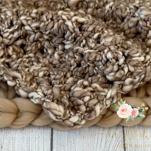 May include: A close-up of a brown and white chunky knit blanket with a soft, textured look. The blanket is made of thick yarn and has a loose, open weave.