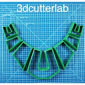 Puede incluir: Cortadores de galletas de plástico verde dispuestos sobre una esterilla de corte azul. Los cortadores tienen varias formas geométricas, incluyendo cuadrados, rectángulos y una forma de U. El texto "3dcutterlab" está en letras blancas en la parte superior.