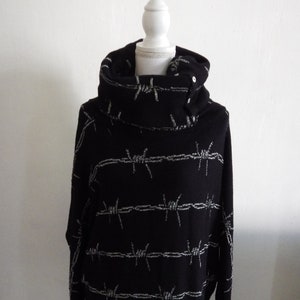 Peut inclure: Pull noir à col montant avec un motif de fil de fer barbelé argenté.