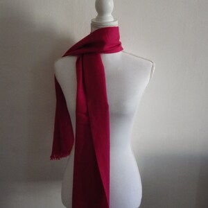 May include: A bright pink scarf with fringed edges draped on a white mannequin.