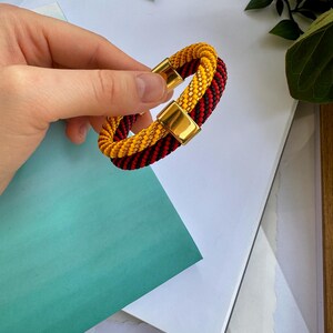 May include: A braided bracelet with red and yellow beads and a gold clasp.