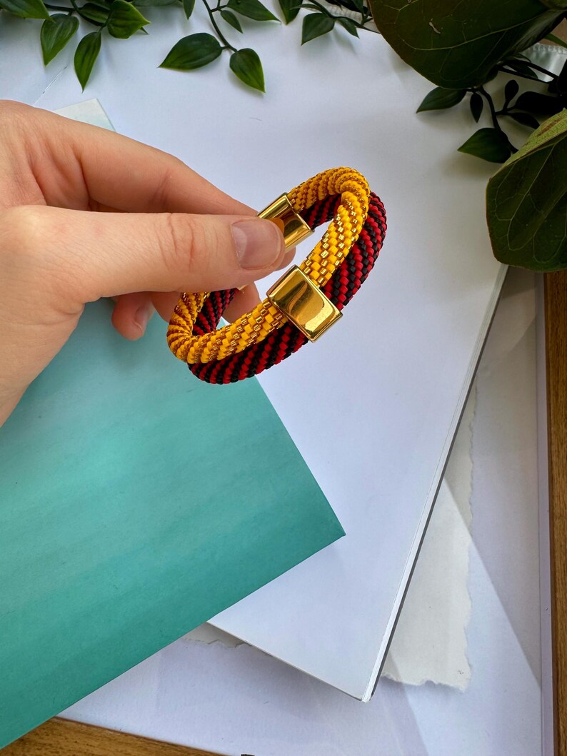 May include: A braided bracelet with red and yellow beads and a gold clasp.