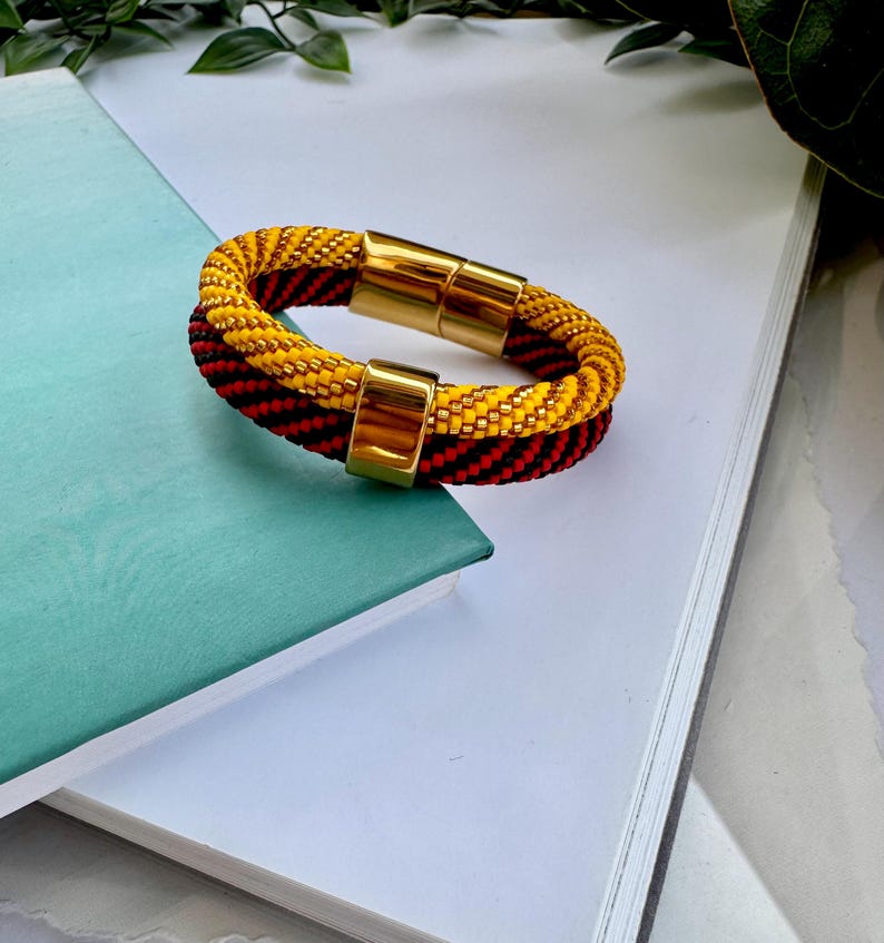 May include: A yellow and black beaded bracelet with a gold magnetic clasp. The bracelet is made of small beads and has a woven design.