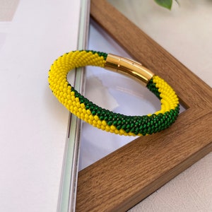 May include: A yellow and green beaded bracelet with a gold magnetic clasp.