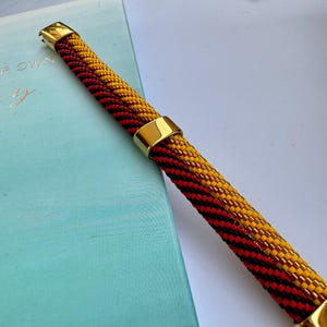 May include: A beaded bracelet with black, red, and yellow beads. The bracelet has two gold metal clasps.