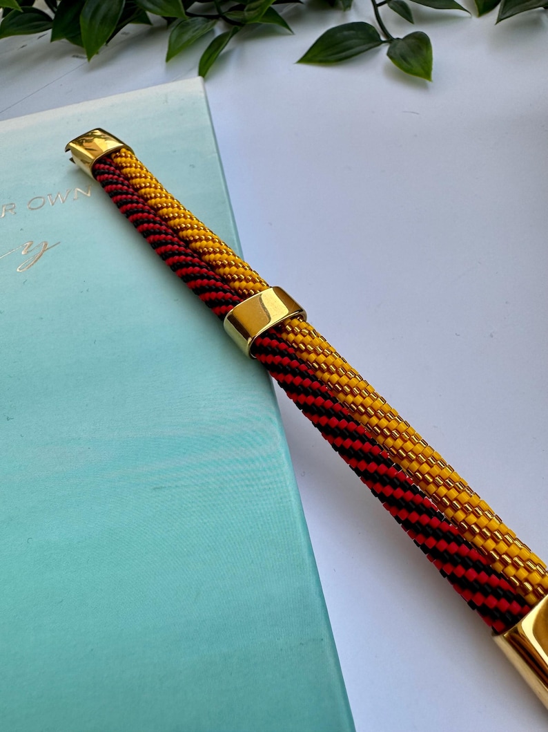May include: A beaded bracelet with black, red, and yellow beads. The bracelet has two gold metal clasps.