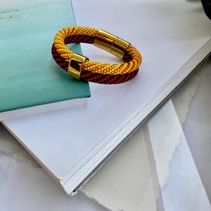 May include: A yellow and red beaded bracelet with a gold magnetic clasp. The bracelet is lying on a white surface.