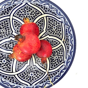 Peut inclure: Une assiette décorative en céramique avec un motif géométrique bleu et blanc contient quatre grenades mûres. Les grenades sont d'un rouge vif, et l'assiette a un bord bleu foncé. Le diamètre de l'assiette est d'environ 30 cm.
